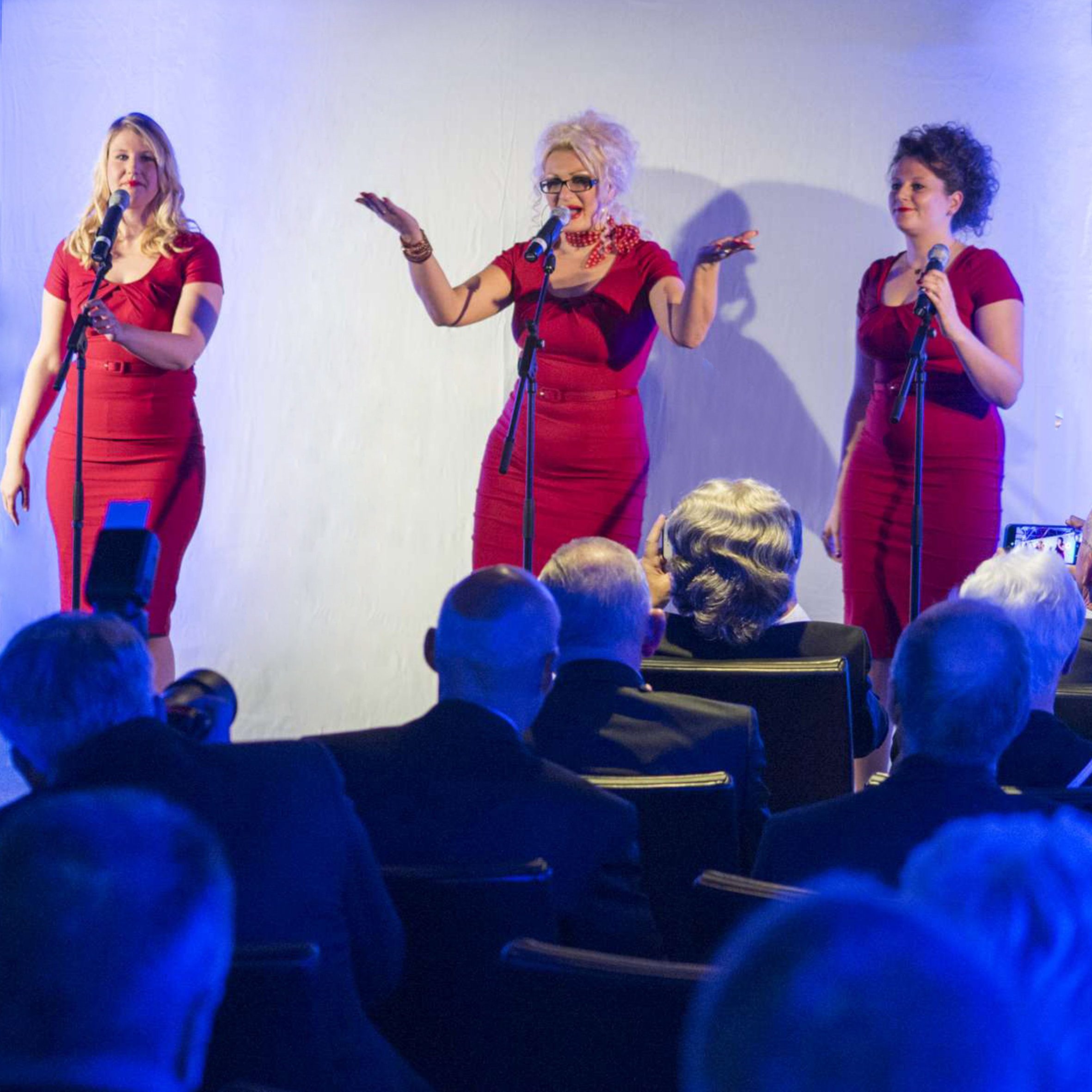 Foto 90. Jubiläum der PVS, Impression des musikalischen Programmes, drei Sängerinnen in roten Kleidern mit Publikum im Vordergrund