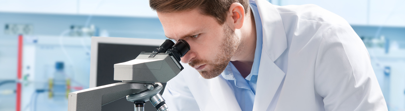 Foto eines Mannes im weißen Kittel, der durch ein Mikroskop schaut.