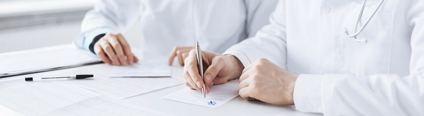 Foto zweier Ärzte in weißen Kitteln an einem Schreibtisch, beide füllen Unterlagen aus.