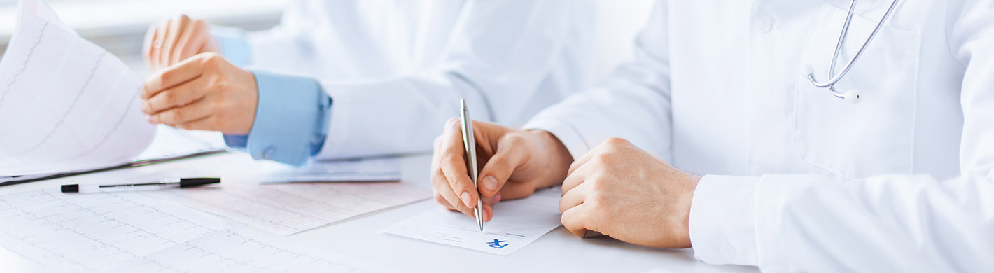Bild von zwei Ärzten im weißen Kittel am Schreibtisch, die an Unterlagen arbeiten und Dokumente ausfüllen.